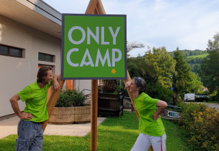 Zwei Personen in grünen Shirts stehen neben einem 'ONLY CAMP'-Schild auf dem Camping l'Orée d'Alsace in Frankreich.