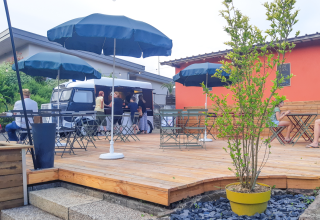Terraza al aire libre con mesas, sombrillas, visitantes y un foodtruck en Onlycamp Camping l'Orée d'Alsace en Grand Est, Francia.