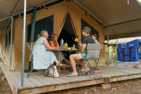 Cuatro personas se relajan frente a una tienda tipo safari en Onlycamp Camping l'Orée d'Alsace en Francia.