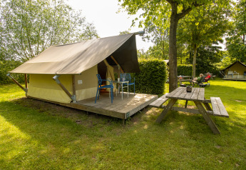 Safari Trekking tent op een groene camping met houten terras, stoelen en picknicktafel in de buurt.