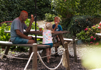 Un uomo e due bambini mangiano un gelato a un tavolo di legno vicino alla Safari Trekking tent in Olanda.