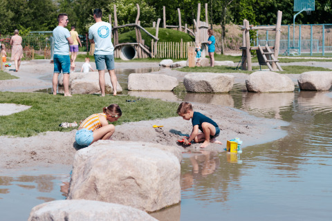 Kinderen spelen aan een vijver in een buitenspeeltuin bij Camping 't Geuldal, Nederland.