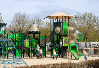 Kinderen spelen op een grote speeltuin met glijbanen en klimrekken op een camping in Nederland, lente.