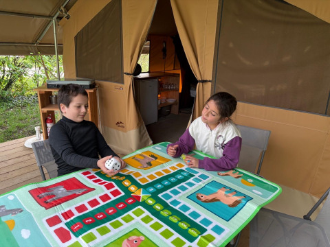 To børn spiller brætspil i et safari telt ved Onlycamp Camping le Champ d'Eté, Ponza teltet, i Frankrig.