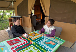 Deux enfants jouent à un jeu de société dans la tente safari Ponza au Onlycamp Camping le Champ d'Eté en France.