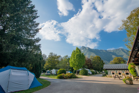 Camping met tenten en caravans omgeven door bomen en bergen onder blauwe lucht in Auvergne-Rhône-Alpes.
