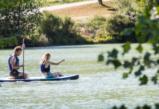Deux personnes font du paddle sur le lac au camping Onlycamp Le Lac de Roybon en Auvergne-Rhône-Alpes.