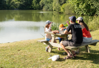 Familie macht ein Picknick am See im Onlycamp Camping Le Lac de Roybon, umgeben von Natur in Auvergne-Rhône-Alpes.