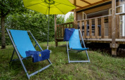 Deux chaises longues bleues et un parasol jaune devant un lodge au Seasonova Camping Le Plan d’Eau en France.