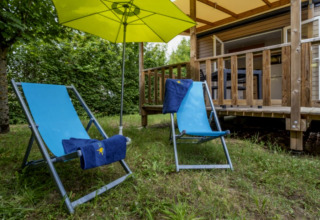 Deux chaises longues bleues et un parasol jaune devant un lodge au Seasonova Camping Le Plan d’Eau en France.