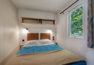 Room with double bed, nightstands, window, and shelves at a lodge in Seasonova Camping Le Plan d’Eau, France.