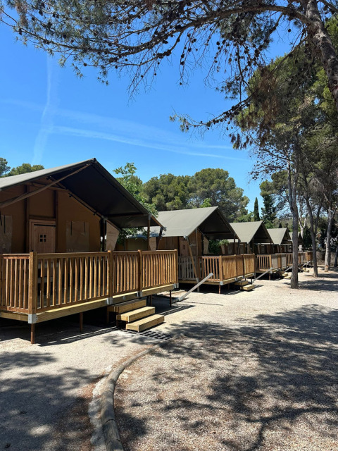 Safari tents called 'Nomad' at Vilanova Park Campsite in Spain, set among trees under a clear blue sky.