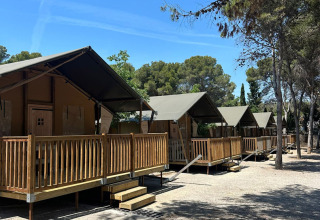 Safari tents called 'Nomad' at Vilanova Park Campsite in Spain, set among trees under a clear blue sky.