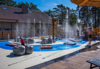 Zona de juegos acuáticos junto a un lodge, con fuentes de agua, estructuras y niños jugando al sol.