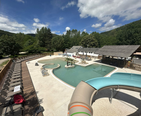 Outdoor swimming pool with water slide and sun loungers at Flower Camping Le Pont du Tarn in Occitanie, France.