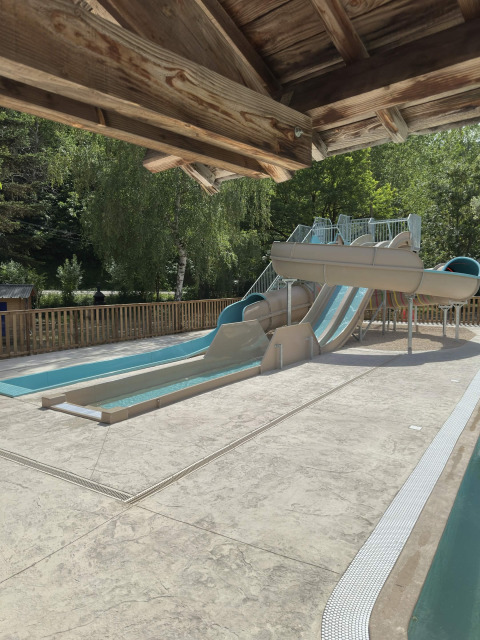 Outdoor swimming pool with water slides under a wooden roof, surrounded by lush trees in southern France.
