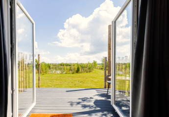 Vue depuis la Tiny House à De Kremmer, Pays-Bas, avec portes vitrées ouvertes sur terrasse et verdure.