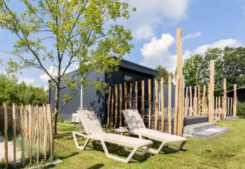 Espace extérieur du Tiny House à De Kremmer, Pays-Bas, avec transats, arbres et clôture en bois.