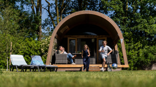 Kinderen spelen voor een grote safari tent lodge XL met sanitair terwijl een volwassene relaxt op het terras.