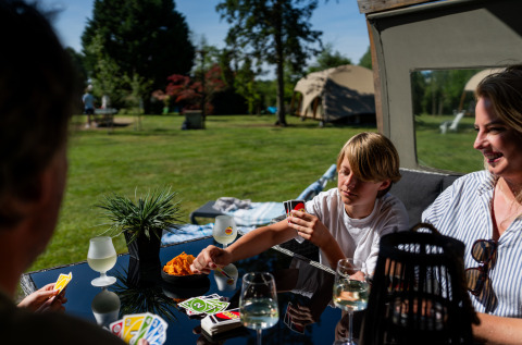 Gezin speelt kaartspel buiten aan safaritent met snacks en drankjes op vakantiecentrum in Nederland.