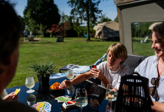 Familie spielt Karten draußen vor einer Safari-Lodge mit Snacks und Getränken im Ferienzentrum.