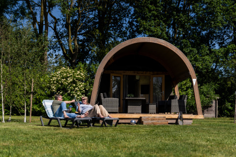 Twee mensen ontspannen op ligbedden voor een safaritent lodge bij Holiday center 't Schuttenbelt in Nederland.