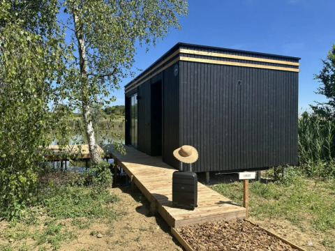Cabina nera Cabane Spa «Loggy» al Domaine des Feuilles, Francia, con valigia e cappello sulla passerella.