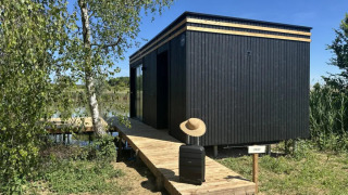 Cabaña negra Cabane Spa «Loggy» en Domaine des Feuilles, Francia, con maleta y sombrero en la pasarela.