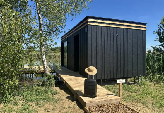 Cabina nera Cabane Spa «Loggy» al Domaine des Feuilles, Francia, con valigia e cappello sulla passerella.
