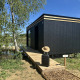 Cabina nera Cabane Spa «Loggy» al Domaine des Feuilles, Francia, con valigia e cappello sulla passerella.