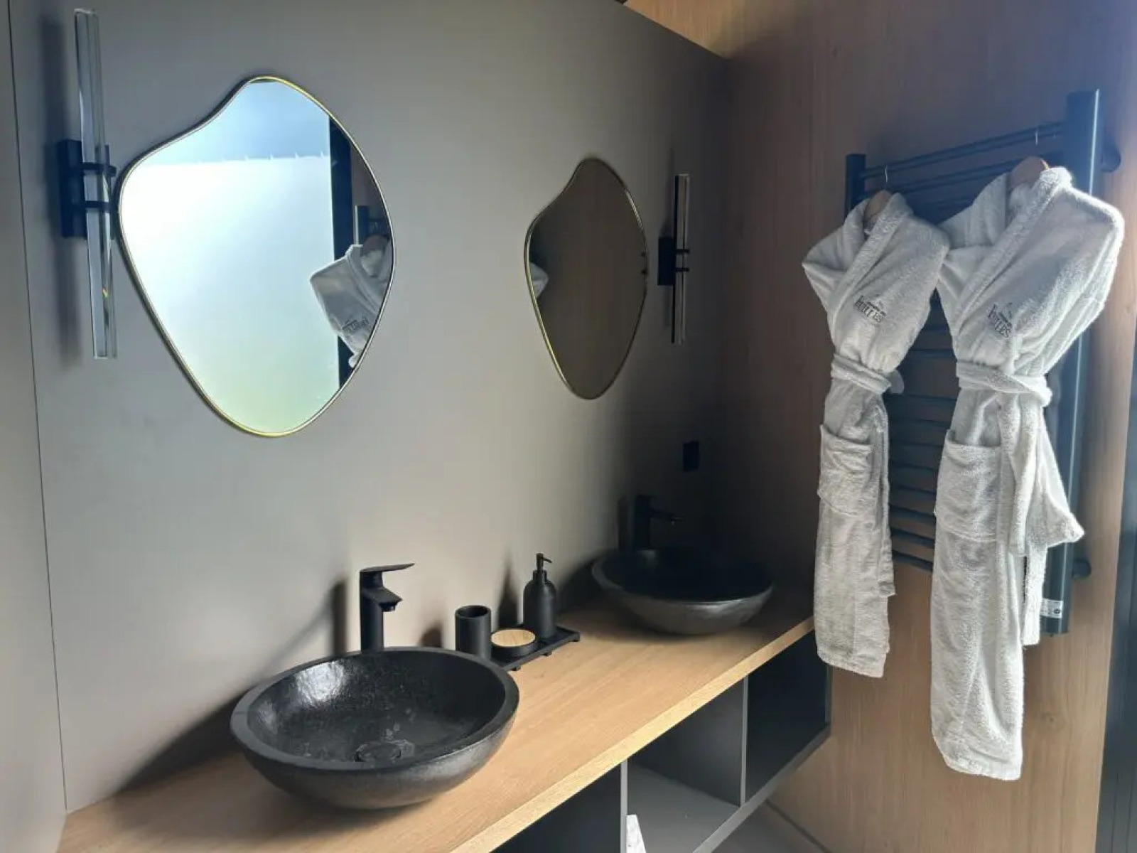 Moderne badkamer met twee unieke spiegels, zwarte wastafels en badjassen in Cabane Spa Loggy, Frankrijk.