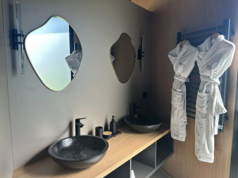 Bagno moderno con due specchi unici, lavandini neri e accappatoi presso Cabane Spa Loggy in Francia.