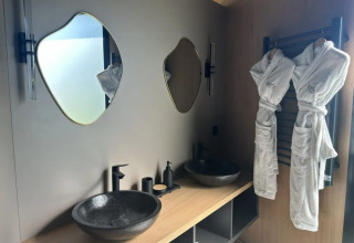 Bagno moderno con due specchi unici, lavandini neri e accappatoi presso Cabane Spa Loggy in Francia.
