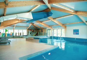 Binnenzwembad bij een lodge met een glijbaan, ligstoelen en een kleurrijke kinderhoek op de achtergrond.
