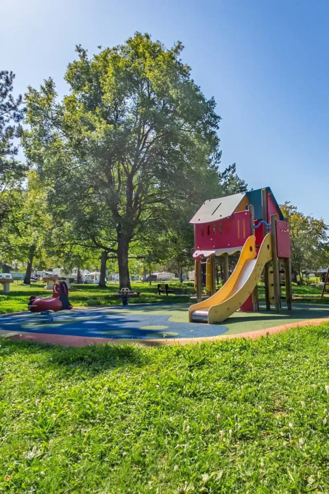 Playground at Seasonova Camping Le Brabois, Grand Est, France, with slide, trees and blue sky on a sunny day.