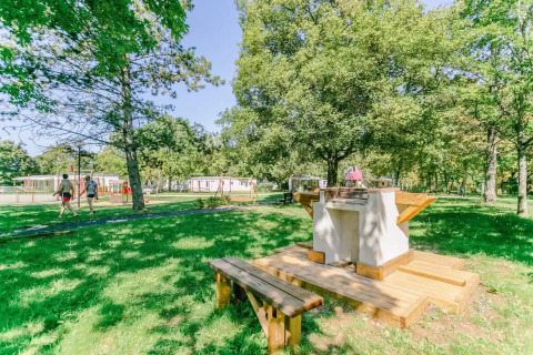 Außenbereich mit Grill und Holzbänken im Seasonova Camping Le Brabois, Grand Est, Frankreich.