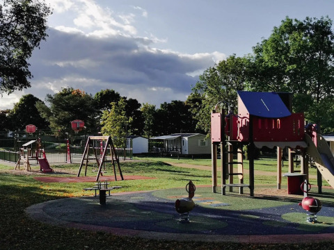 Playground at Seasonova Camping Le Brabois, Grand Est, France, with slides, swings, trees, and cabins visible.