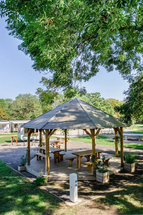 Holzpavillon mit Bänken in grüner Umgebung im Seasonova Camping Le Brabois, Grand Est, Frankreich.