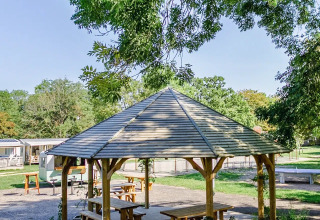 Pabellón de madera con bancos en un parque verde en Seasonova Camping Le Brabois, Grand Est, Francia.