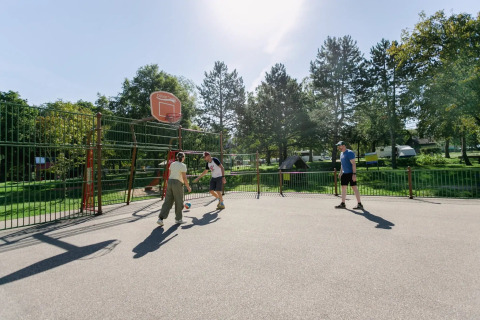 Personas jugando baloncesto en una pista al aire libre bajo el sol en Seasonova Camping Le Brabois, Grand Est, Francia.