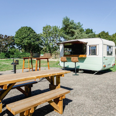 Draußen-Szene mit Holzbänken, Tischen und einem Imbisswagen im Camping Le Brabois, Grand Est, Frankreich.