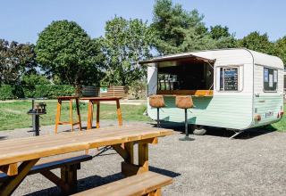 Scène extérieure avec bancs, tables en bois et une caravane snack au camping Le Brabois, Grand Est, France.
