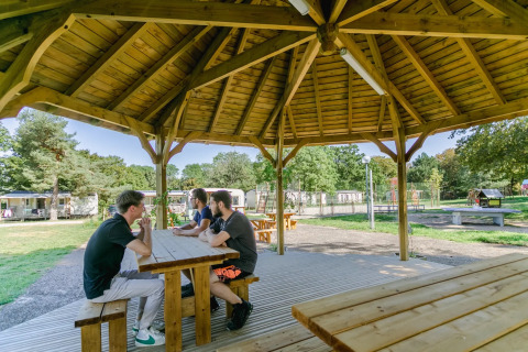 Quatre jeunes hommes assis à une table en bois sous un pavillon au Seasonova Camping Le Brabois, Grand Est, France.