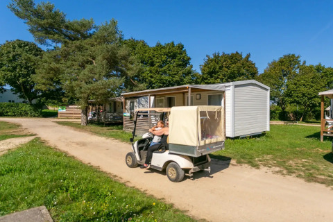 Ein Golfwagen fährt an Mobilheimen im Seasonova Camping Le Brabois im sonnigen Grand Est, Frankreich, vorbei.