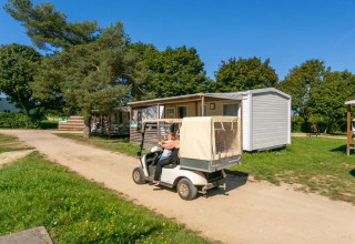 Ein Golfwagen fährt an Mobilheimen im Seasonova Camping Le Brabois im sonnigen Grand Est, Frankreich, vorbei.