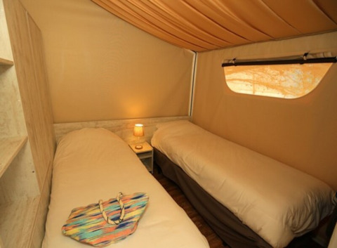 Interno della tenda safari Maasaï Lodge al Seasonova Camping Le Brabois in Francia, con due letti singoli e illuminazione soffusa.