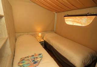 Interno della tenda safari Maasaï Lodge al Seasonova Camping Le Brabois in Francia, con due letti singoli e illuminazione soffusa.