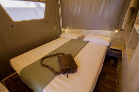 Vista interna di una tenda safari Maasaï Lodge al Seasonova Camping Le Brabois in Francia, con letto rifatto.