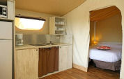 Vista interior de la tienda safari Maasaï Lodge en Seasonova Camping Le Brabois, con cocina y cama doble.