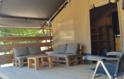 Buitenzitje bij Lodgetent safaritent op Camping Luna del Monte, Italië, met houten meubels en kussens.